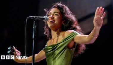 Ed Sheeran in a white shirt playing the guitar with a hazy orange background behind him