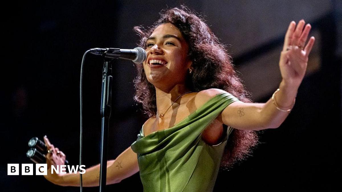 Ed Sheeran in a white shirt playing the guitar with a hazy orange background behind him