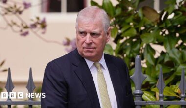 Andrew Mountbatten-Windsor wearing a dark-coloured suit with a white shirt and yellow tie