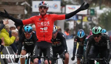 Dorian Godon holds out his arms as he rides his bicycle next to several other competitors