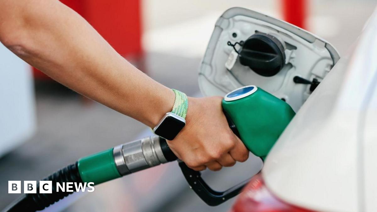 A close up stock image of an arm with a smartwatch with a light green strap putting a green unleaded petrol pump handle in to a car. The car is white.