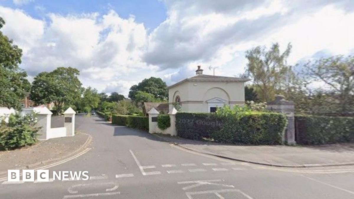 Road junction leading to housing with hedging along both sides of the road.