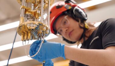 an engineer in blue gloves and safety gear screws a cable into the bottom of a gold-plated dilution refrigerator used to keep quantum computers extremely cold