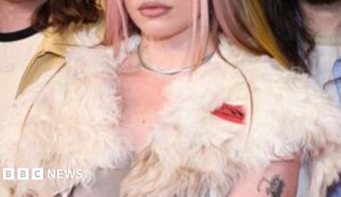 Harry Styles performs at the Brit Awards. He is wearing a grey office shirt and tie combination.