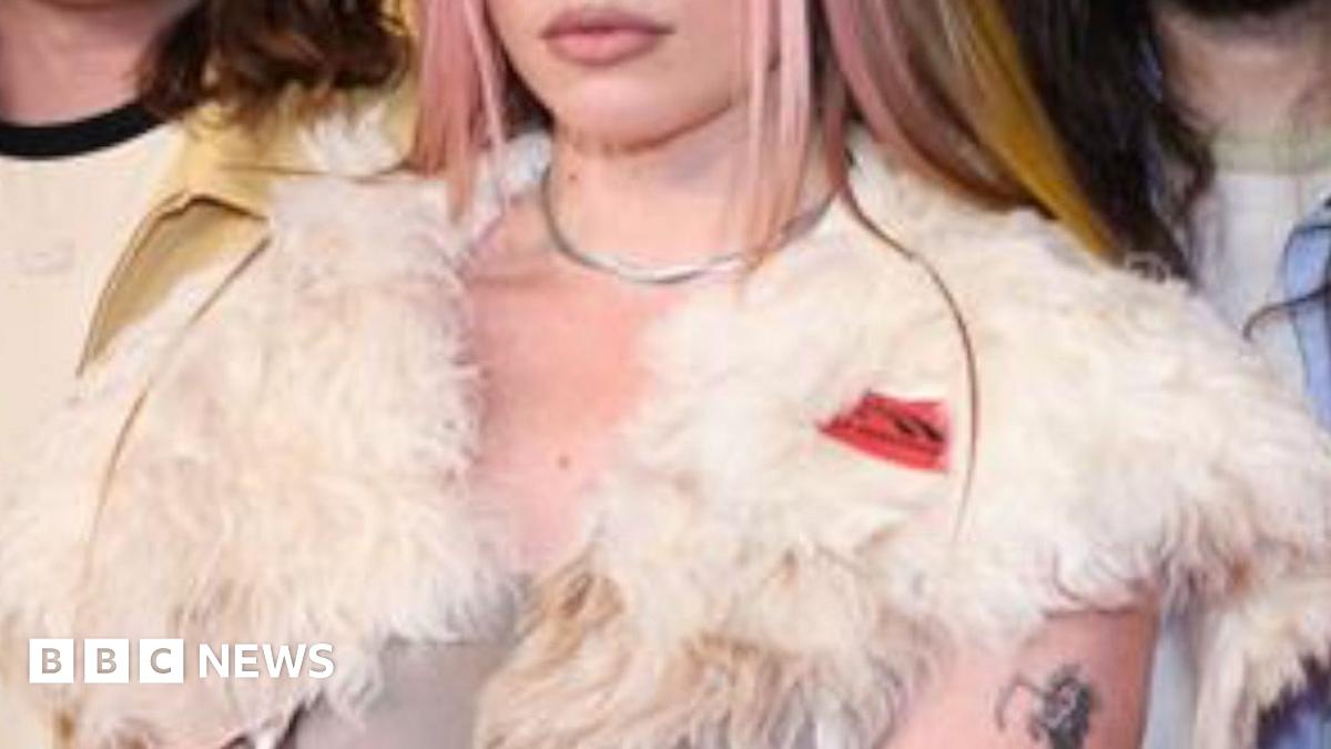 Harry Styles performs at the Brit Awards. He is wearing a grey office shirt and tie combination.