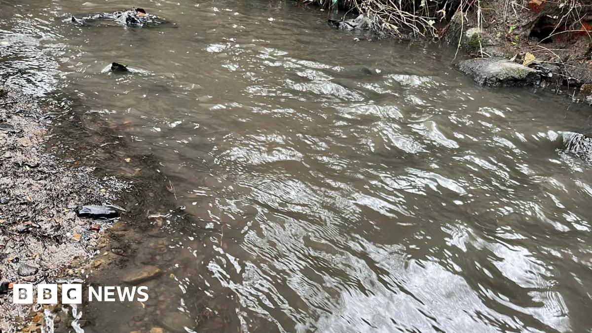 The water of a small beck has become a dark grey and black colour. It is opaque and the gravel at the bottom of the water cannot be seen.