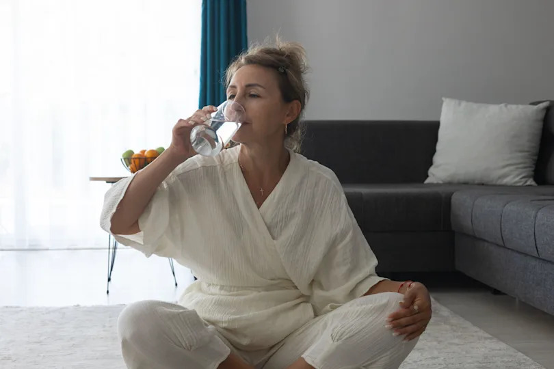 A middle-aged woman sitting on the floor drinking water 