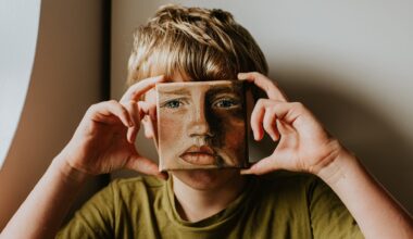 A young lad covers his face with a small oil painting of himself. The expression on the painting is serious.