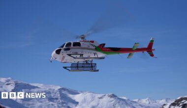 Stock image of a female climber wearing a backpack hanging onto a rock