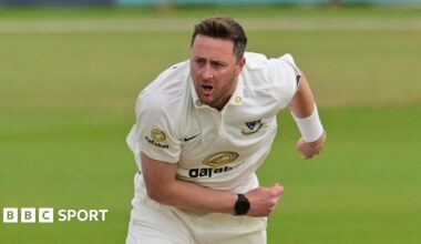 Ollie Robinson playing for Sussex and slightly hunched over with his right arm across his front and his left splayed to the back, having just completed a delivery.