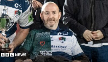 Matt Gallagher sat in an electric wheelchair after a rugby game, posing with the team and his family