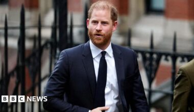 Prince Harry, who has ginger hair and a beard, wears a dark suit and tie with a white shirt as he is seen walking into the High Court building in London