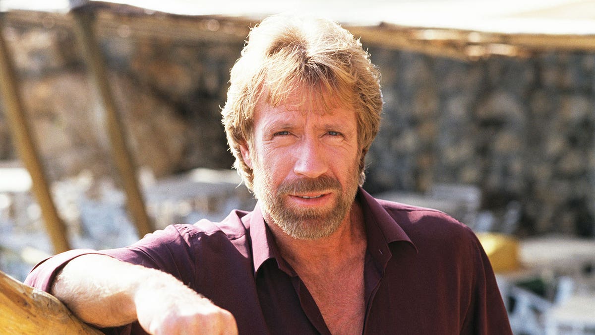 Chuck Norris wearing a burgundy shirt posing in Sicily.