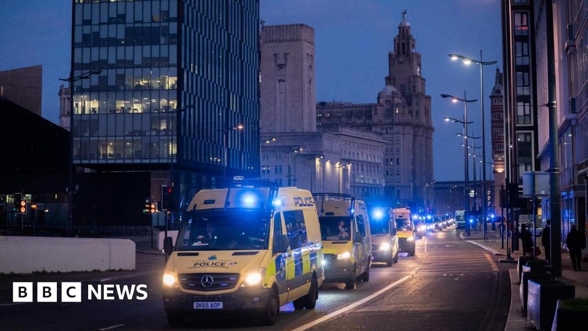A convoy of yellow police vans in front of the Liver Building