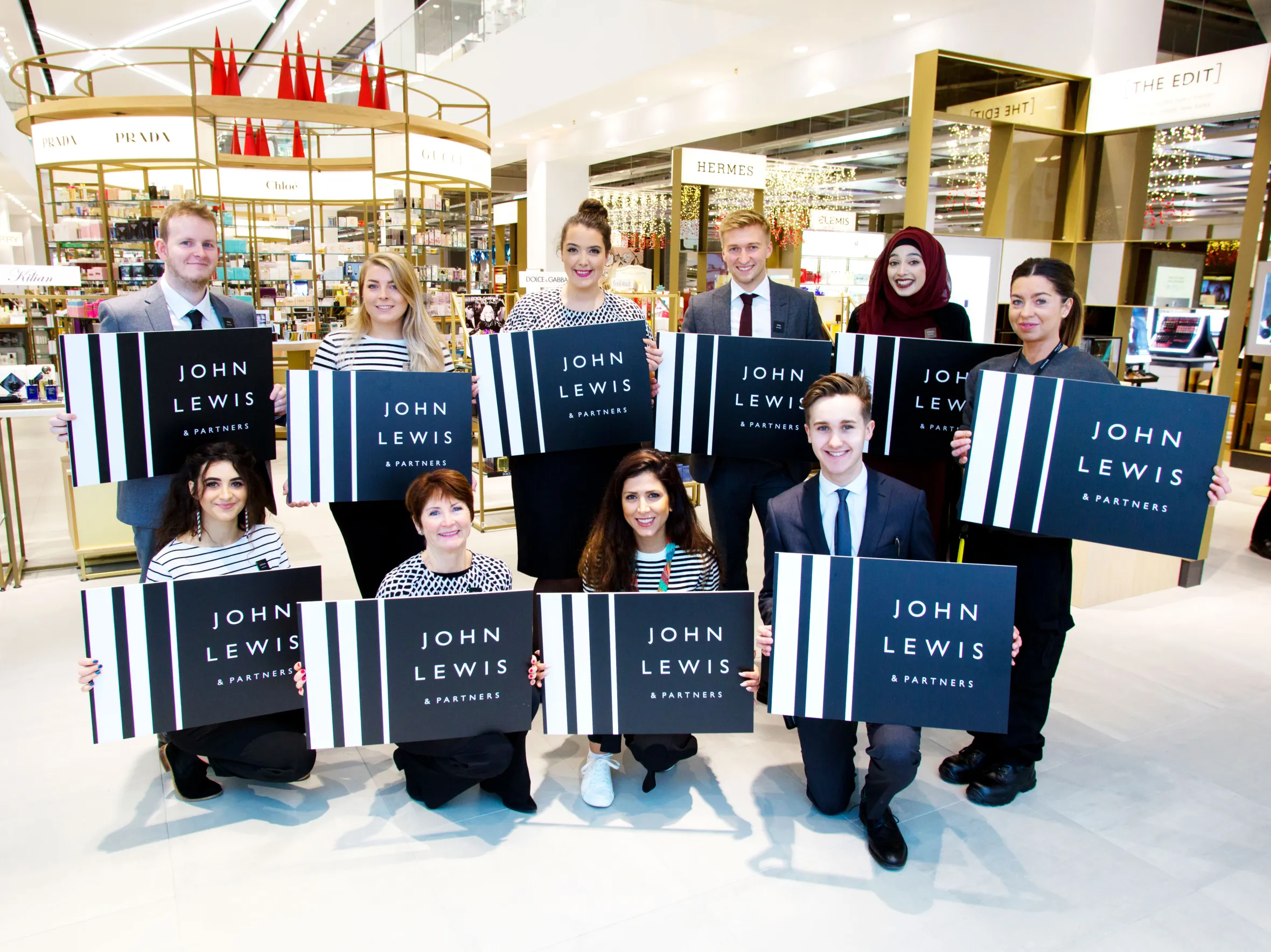 Eleven John Lewis & Partners employees holding "John Lewis & Partners" signs in the Cheltenham store.