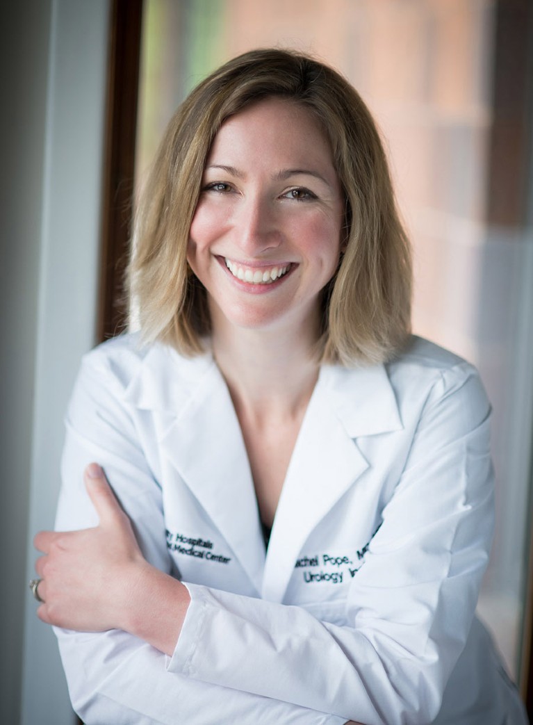 White woman wearing white lab coat smiling to camera.