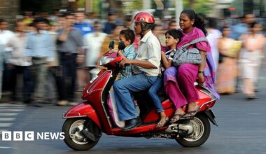A family of four - father, mother and two children, travel on a scooter in India