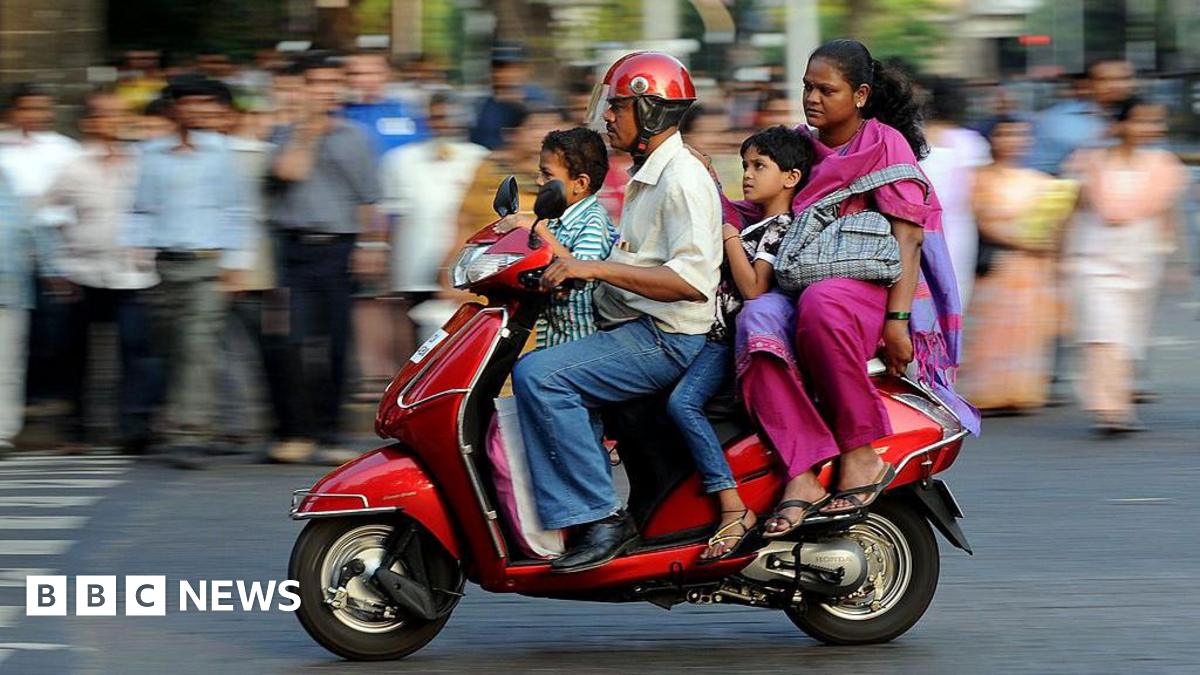 A family of four - father, mother and two children, travel on a scooter in India
