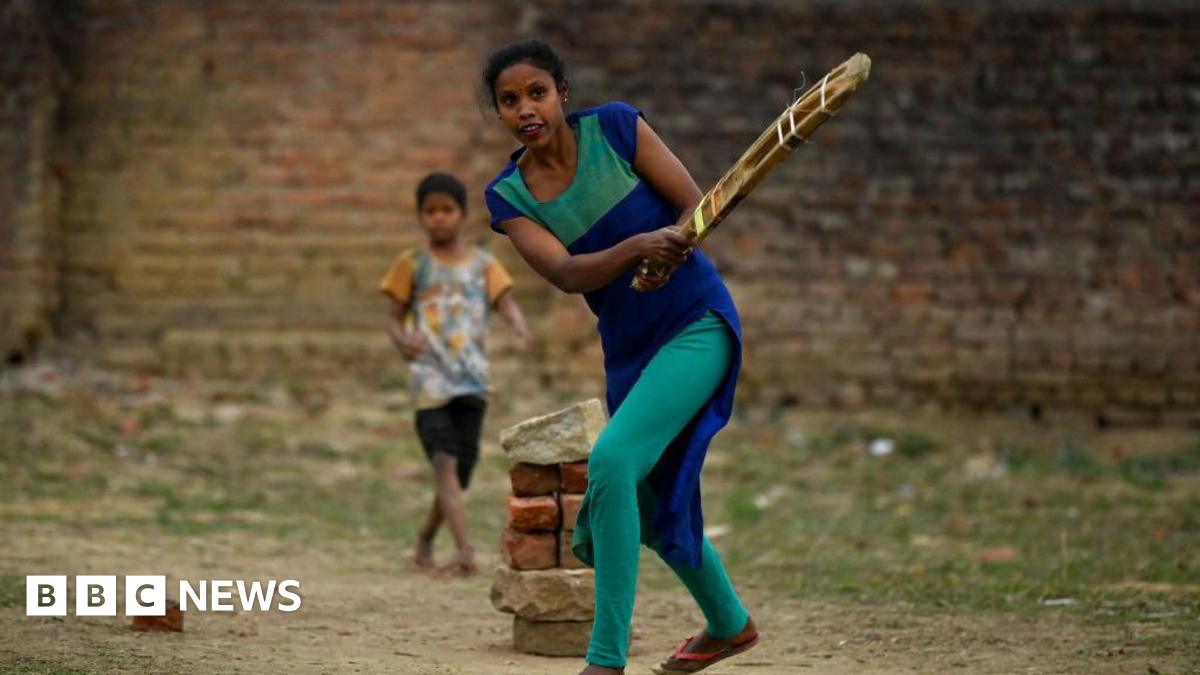 A woman with dark hair and a multiple colour jumper siting on a green sofa inside her living room.