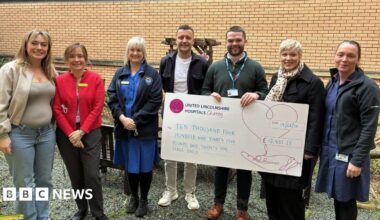 A group of people, including nursing staff, standing in line. Two of the people are holding a giant cheque.