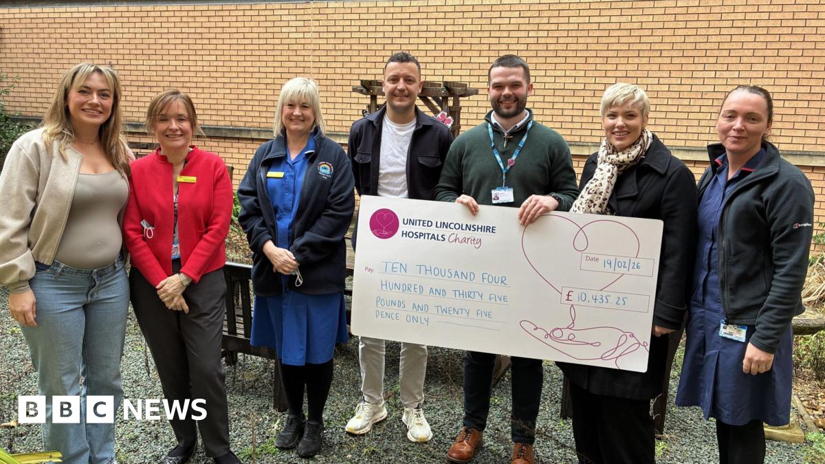 A group of people, including nursing staff, standing in line. Two of the people are holding a giant cheque.