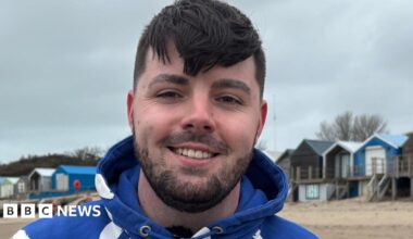 Ruben smiling at the camera, wearing a blue hoodie in front of a row of beach houses