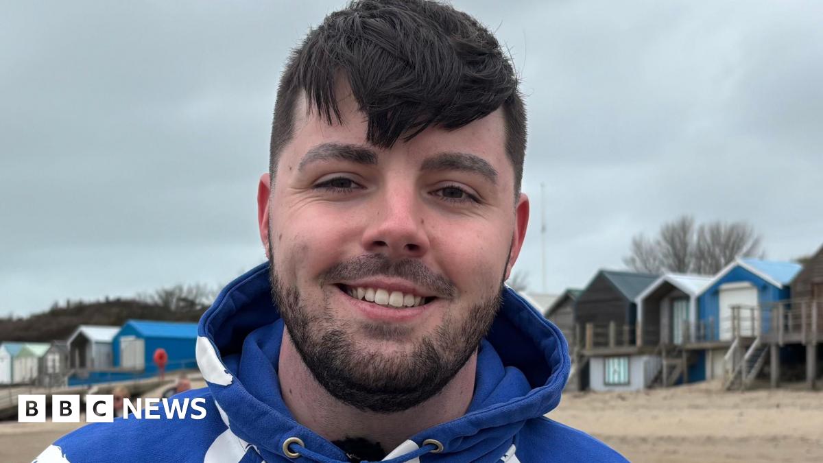 Ruben smiling at the camera, wearing a blue hoodie in front of a row of beach houses