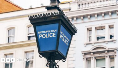 A blue Metropolitan Police lamp post with the words Metropolitan Police in white writing. There's a white building in the background