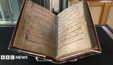 Manuscript printed with medieval English music behind a glass case in a museum.