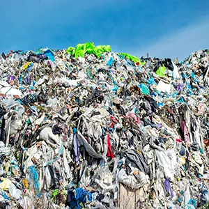 A large mound of waste textiles from donated clothes stretches towards the horizon, showcasing the scale of clothing pollution in the landscape
