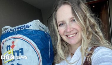 Photo of Laura who has long blonde hair and smiling. She is posing next to the bag of clothes she sent to avoid extra luggage costs.