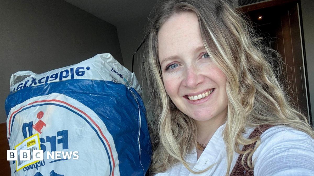 Photo of Laura who has long blonde hair and smiling. She is posing next to the bag of clothes she sent to avoid extra luggage costs.