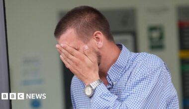 Shaun Thompson, who is wearing a blue and white checkered shirt, covering his face as he leaves court. He has short brown hair.