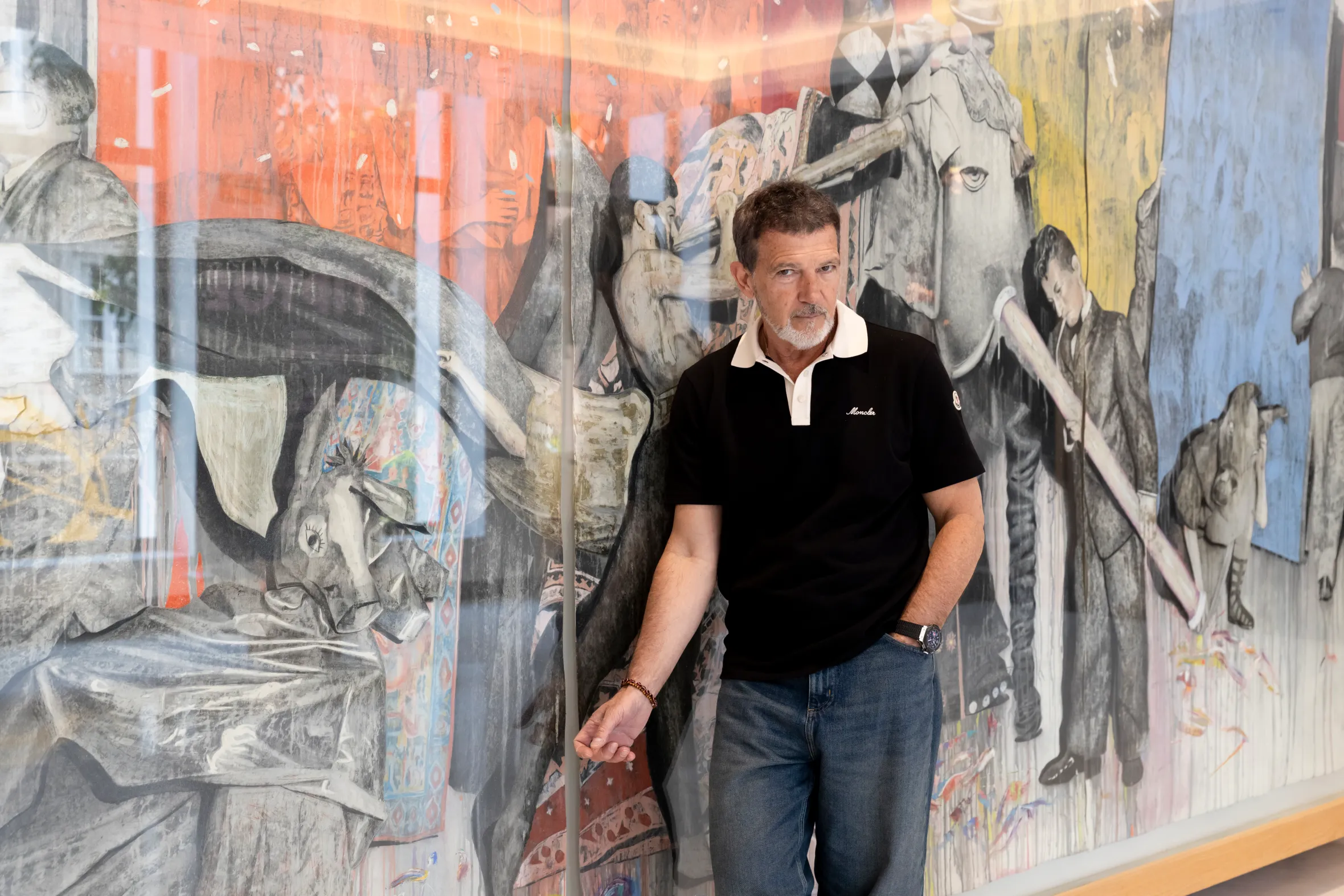 Antonio Banderas standing in front of a colorful, abstract painting.