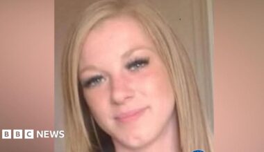 A woman with pink long hair smiling. She is standing next to a wind