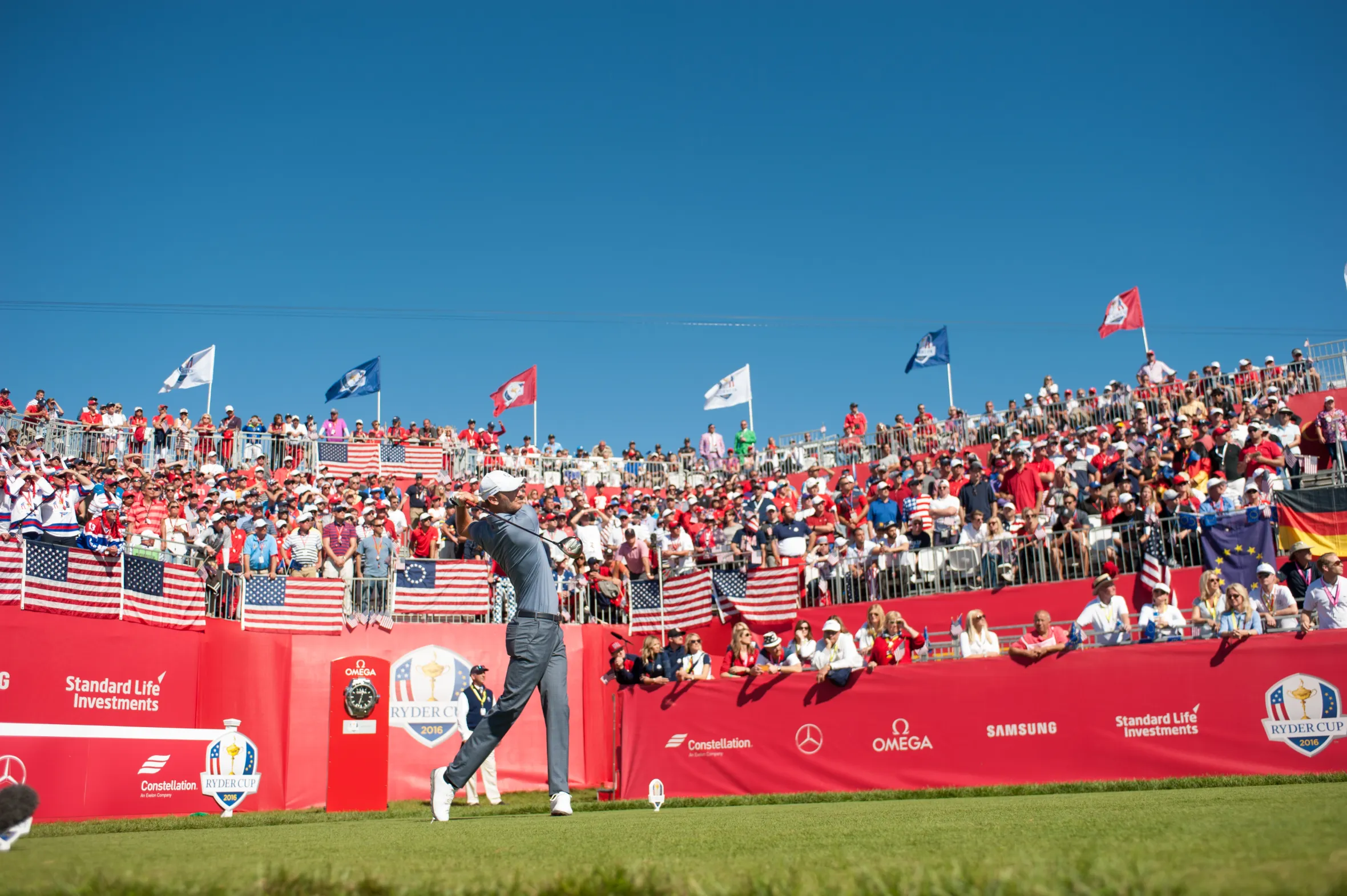 Chris Wood teeing off at the 2016 Ryder Cup, with a large crowd in the background.