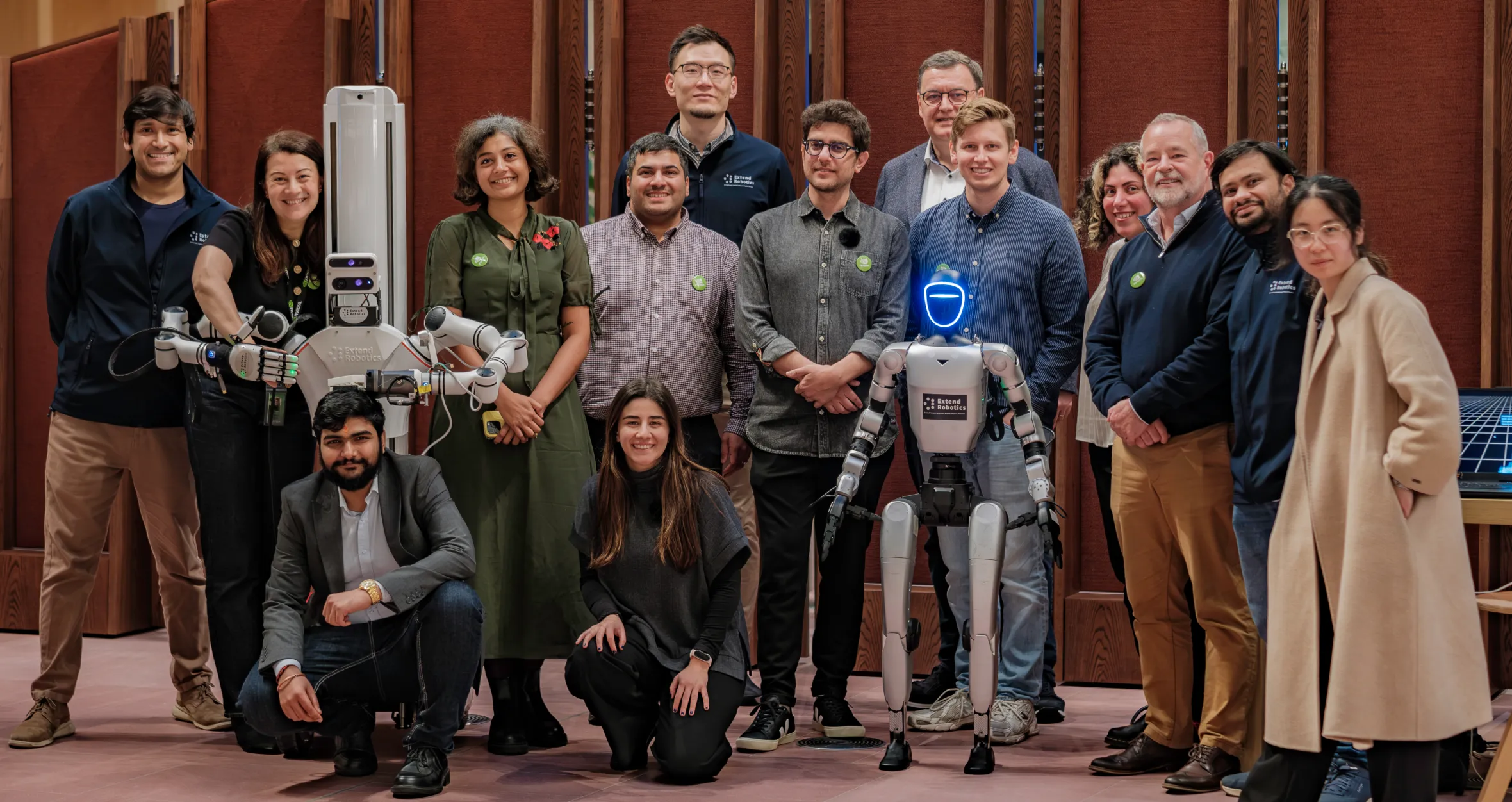 A group of people standing around two robots, smiling at the camera.