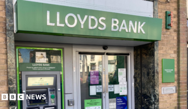 A branch with the words Lloyds Bank in white above the entrance. A cash machine is on the left and there are doors in the middle.