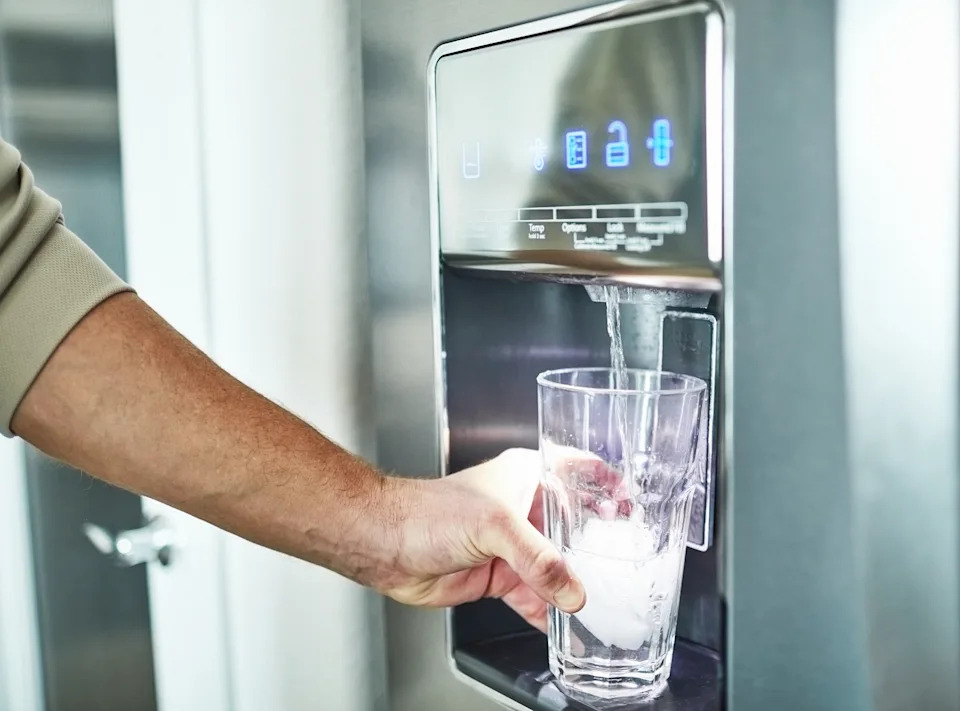 Person filling a glass with ice and water from a modern dispenser