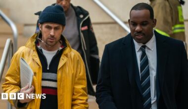 A promotional still from the film shows on the left Gosling as Ryland Grace and on the right Lionel Boyce as security guard Carl as they walk down a set of stairs during the film.