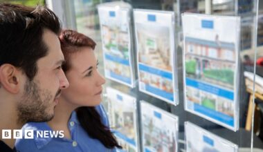 A young man and woman stand alongside each other looking at an estate agents' window.