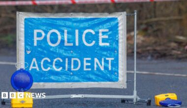 A close-up of a "Police accident" sign, with two blue lights on the ground next to it. One has fallen over.