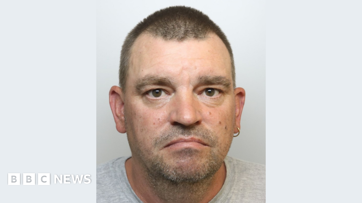A police mugshot of Matthew McKenzie, wearing a grey t-shirt and standing against a plain grey background. He has short brown hair, brown eyes, a silver hoop earring in his left ear and slight stubble. He is looking at the camera with a sad expression.
