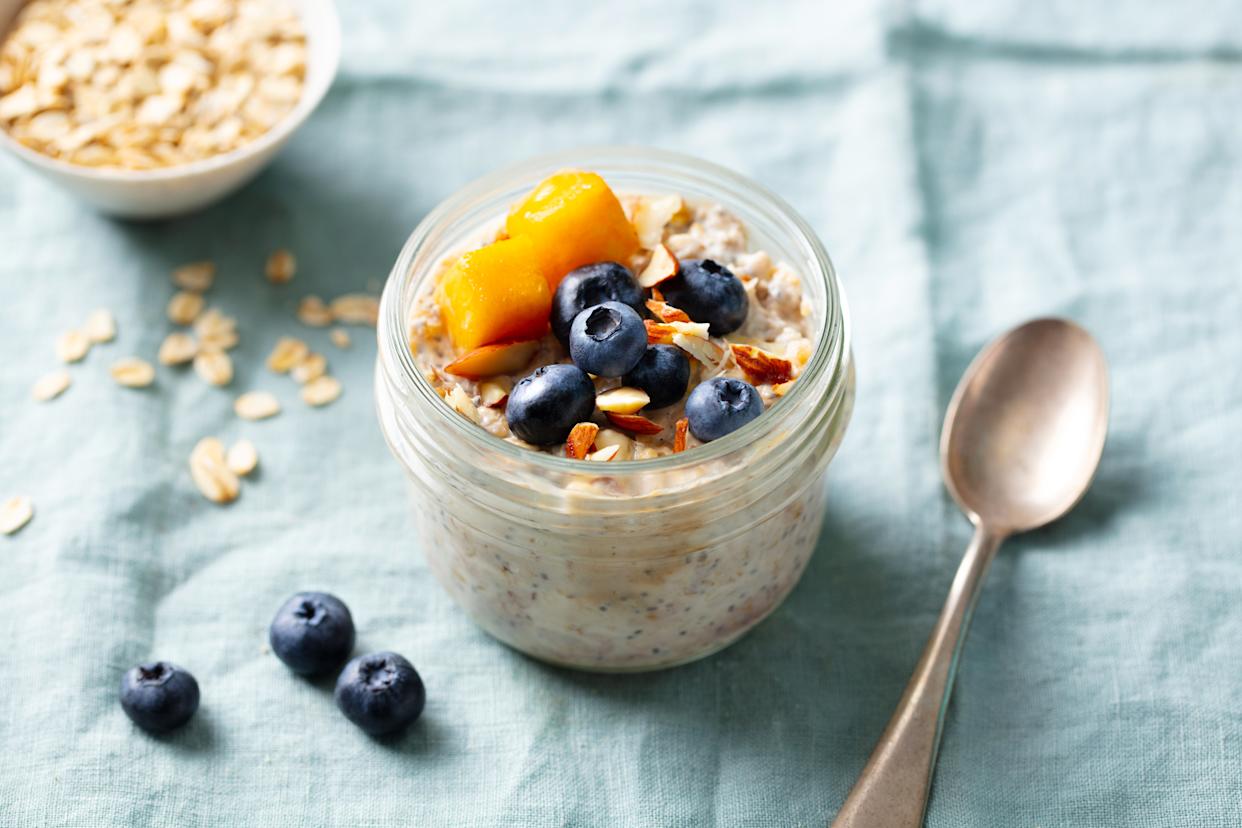 Healthy breakfast. Overnight oats with fresh berries and fruits in glass jars. Blue textile background. Close up.