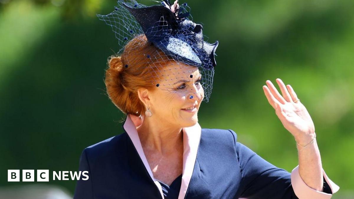 Sarah Ferguson wears a black and white checked jacket with a black top underneath, and is sitting against a black background - plants can just be seen at the side. Her red hair is pushed back with a thin black headband and she has a neutral expression on her face