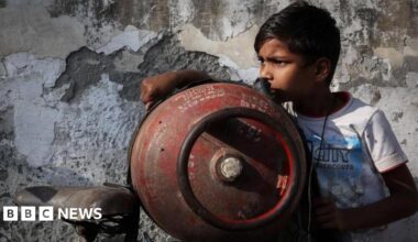 A boy stands next to an empty LPG cylinder tied to a bicycle as he waits outside a gas agency
