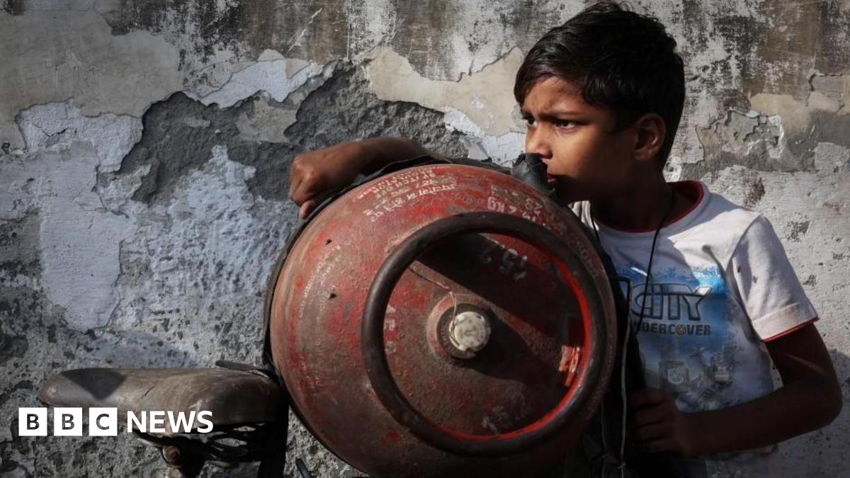 A boy stands next to an empty LPG cylinder tied to a bicycle as he waits outside a gas agency