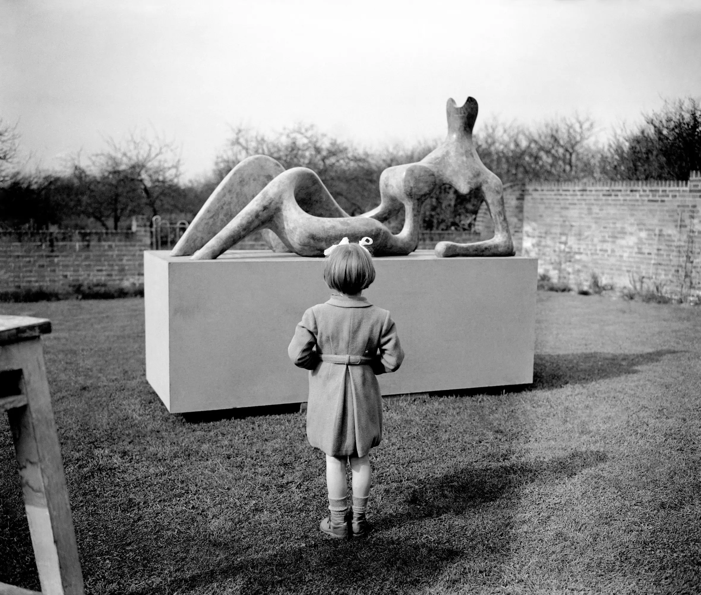 Mary Moore, daughter of sculptor Henry Moore, surveys a reclining figure sculpture in a garden.