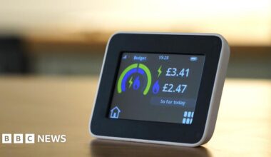 A small smart electricity meter on a table. It has a display that shows a graphic in blue and green contrasting the budget vs the cost of the energy used so far.