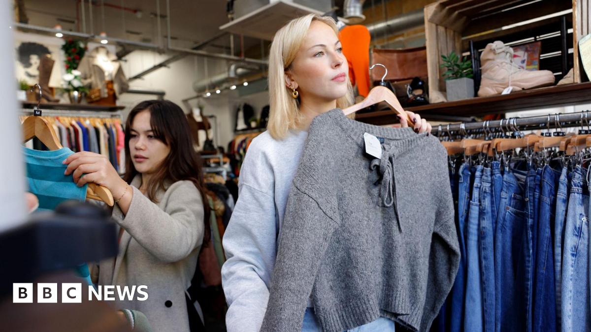 A young blonde woman in a shop holding a grey jumper up against herself